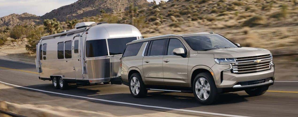 A tan 2023 Chevy Suburban is shown towing an Airstream on an open road.