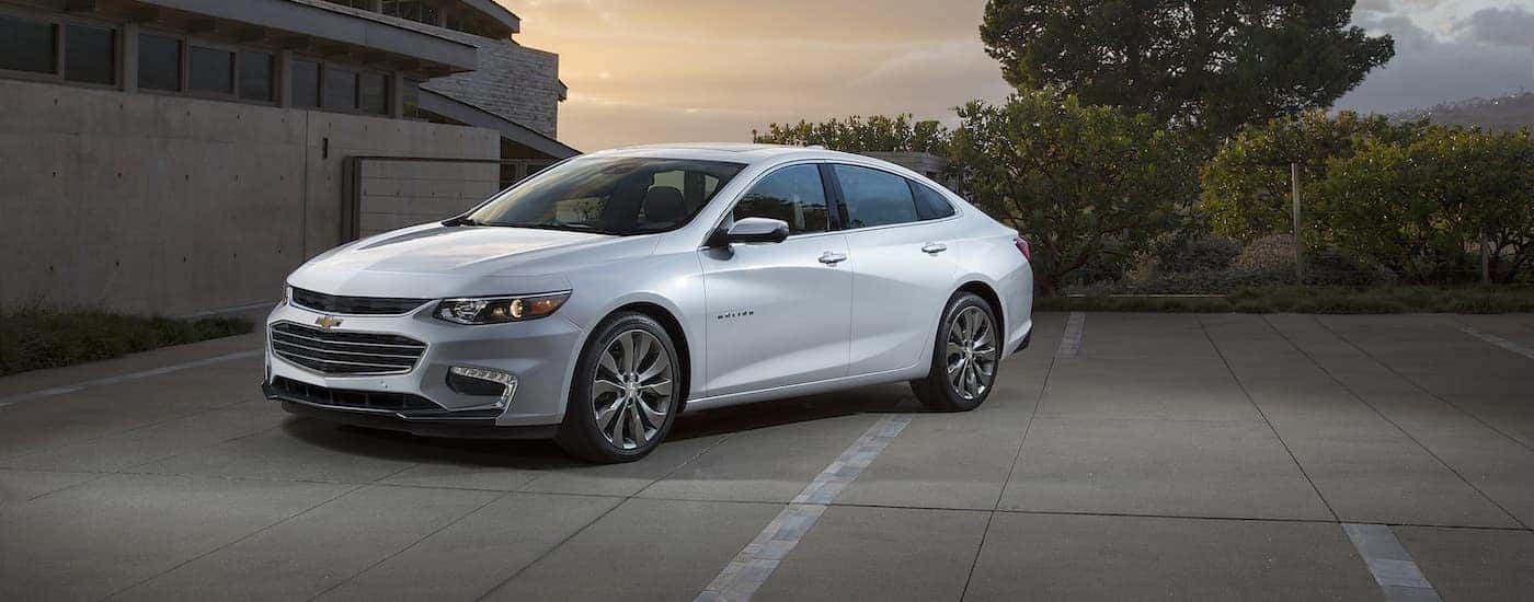 A white 2016 Chevy Malibu is shown parked on concrete after leaving a Chevrolet Malibu dealer.