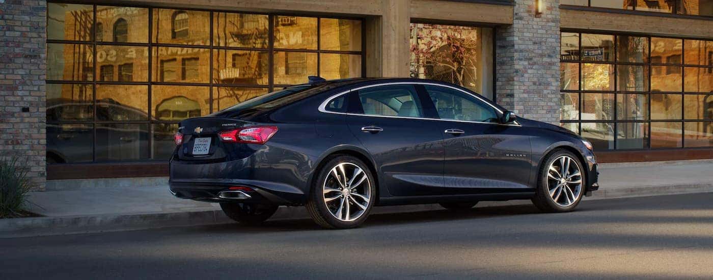 A dark blue 2022 Chevy Malibu is shown parked in front of a glass and brick building.