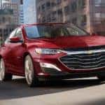 A red 2022 Chevy Malibu is shown driving on a city street after leaving a Chevrolet Malibu dealer.