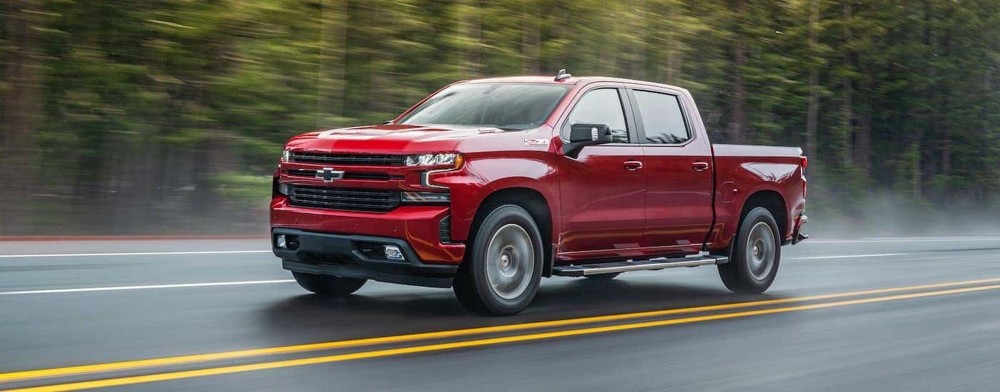 A red 2020 Chevy Silverado 1500 is shown from the side driving on a tree-lined road.