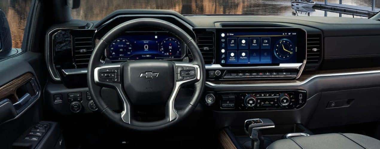 The black interior of a 2023 Chevy Silverado 1500 shows the steering wheel and infotainment screen.