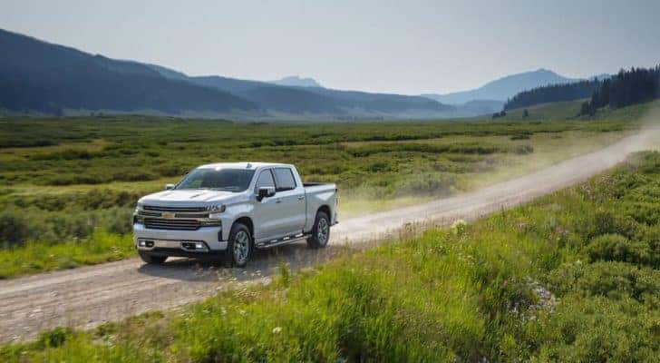 One of the most popular used Chevrolet trucks, a silver 2019 Chevy Silverado 1500 High Country, is shown driving on a dirt trail.