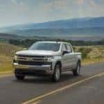 One of the most popular used Chevrolet trucks, silver 2019 Chevy Silverado 1500 LT, is shown driving on an open road.
