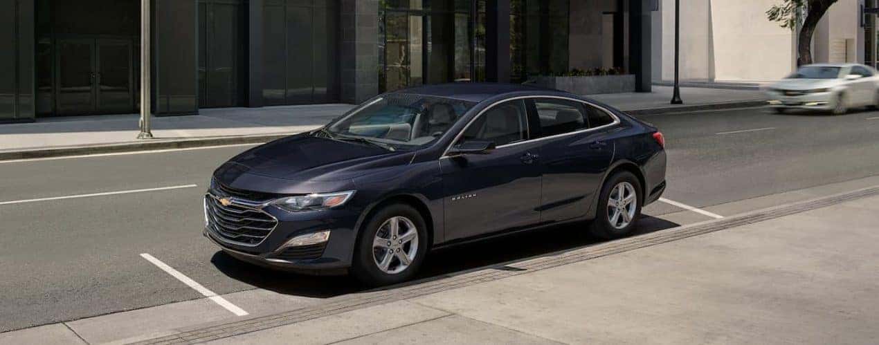 A blue 2023 Chevy Malibu is shown from the side parked on a city street.