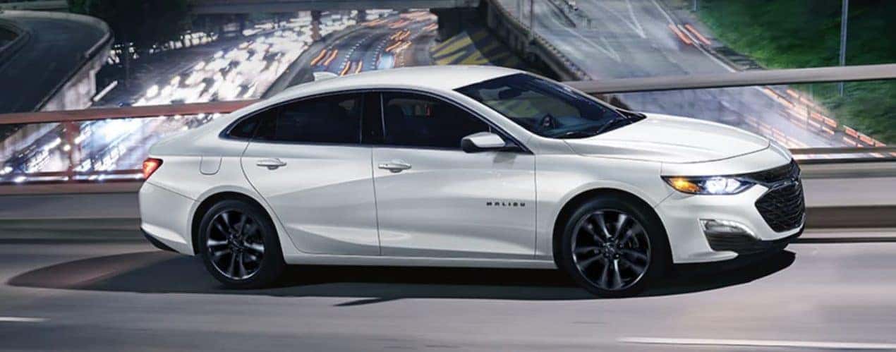 A white 2023 Chevy Malibu is shown from the side driving at night.