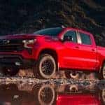 A red 2023 Chevy Silverado 1500 Z71 Trail Boss parked near water and mountains