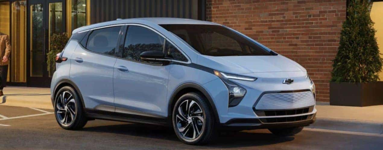 A blue 2023 Chevy Bolt EV is shown parked in front of a brick wall.