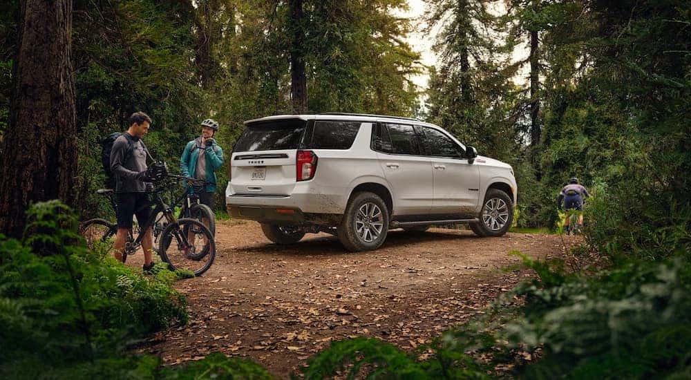 A white 2022 Chevy Tahoe Z71 parked in the woods with bicyclists nearby