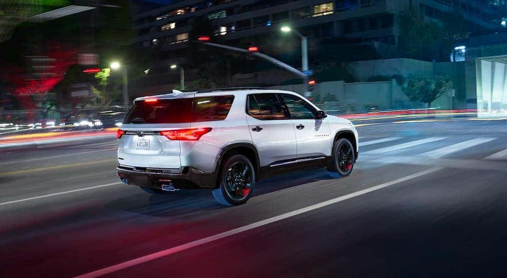 A white 2023 Chevy Traverse Redline driving on a city street at night