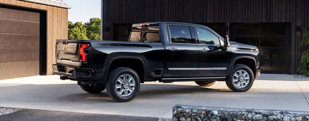 A black 2024 Chevy Silverado 2500 HD High Country is shown from the side in a driveway.