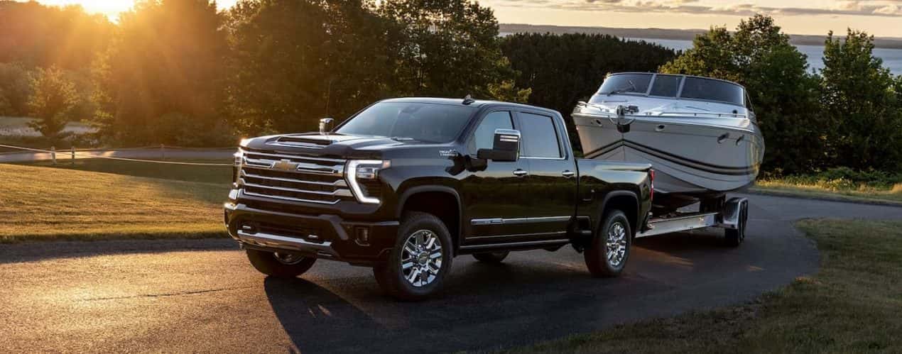 A black 2024 Chevy Silverado 2500 HD High Country is shown towing a boat on a winding road.