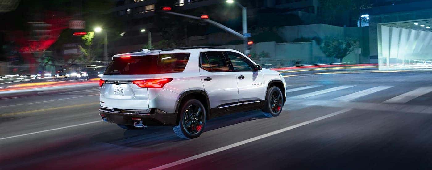 A white 2023 Chevy Traverse Redline is shown driving on a city street at night.