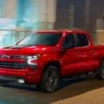 A popular Chevy Silverado for sale in Indianapolis, a red 2023 Chevy Silverado 1500 RST, is shown driving on a city street.