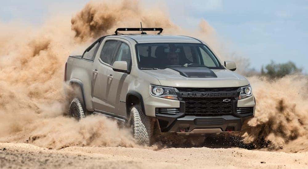 A tan 2021 Chevy Colorado ZR2 is shown from the front at an angle while driving through sand after leaving a Certified Pre-Owned Chevy dealer.