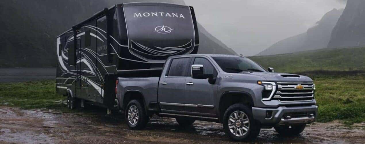 A gray 2024 Chevy Silverado 2500 HD is shown towing a trailer off-road.