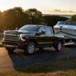 After participating in a 2024 Chevy Silverado 2500 HD vs 2024 Ram 2500 comparison, a black 2024 Chevy Islverado 2500 HD High Country, is shown towing a trailer.