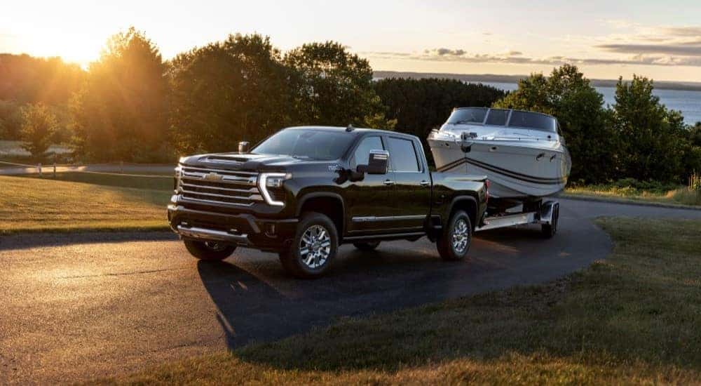 After participating in a 2024 Chevy Silverado 2500 HD vs 2024 Ram 2500 comparison, a black 2024 Chevy Islverado 2500 HD High Country, is shown towing a trailer.