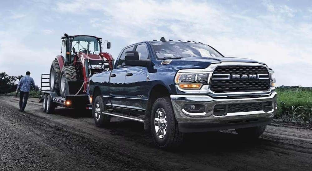 A blue 2024 Ram 2500 Laramie is shown towing a trailer on a dirt road.