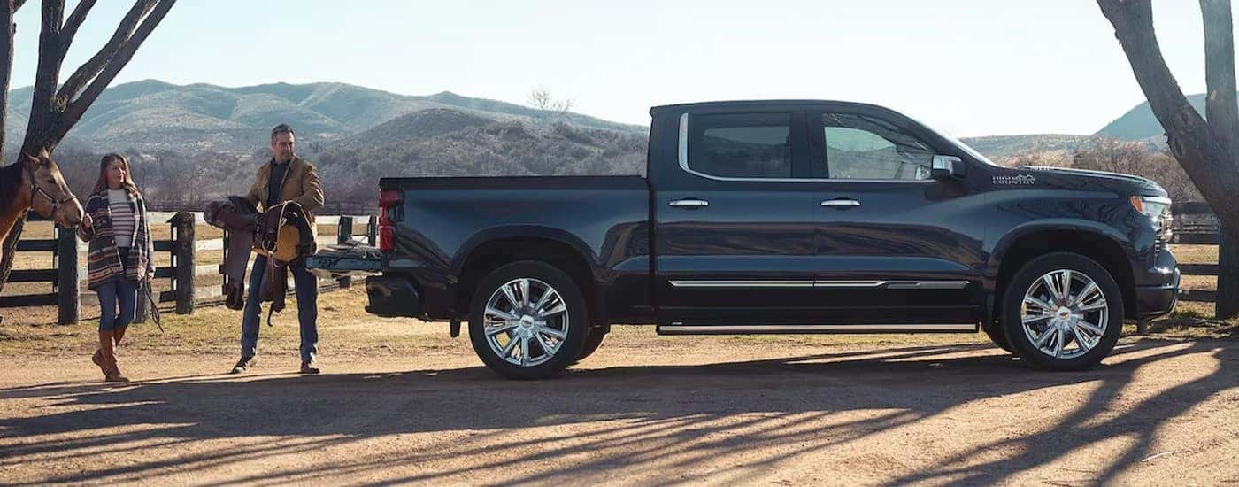 A black 2024 Chevy Silverado 1500 High Country is shown parked near two people and a horse after visiting a Indianapolis Chevy dealer.