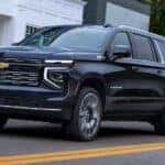 A successor to the 2024 Chevy Suburban, a black 2025 Chevy Suburban, is shown driving in a city.