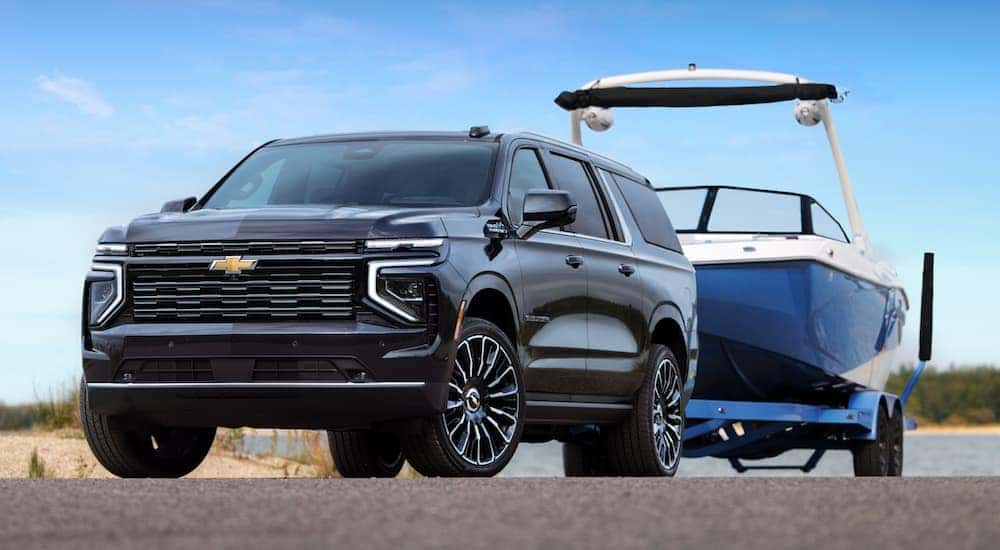 A black 2025 Chevy Suburban is shown towing a boat.
