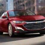 A red 2024 Chevy Malibu driving over a city bridge.