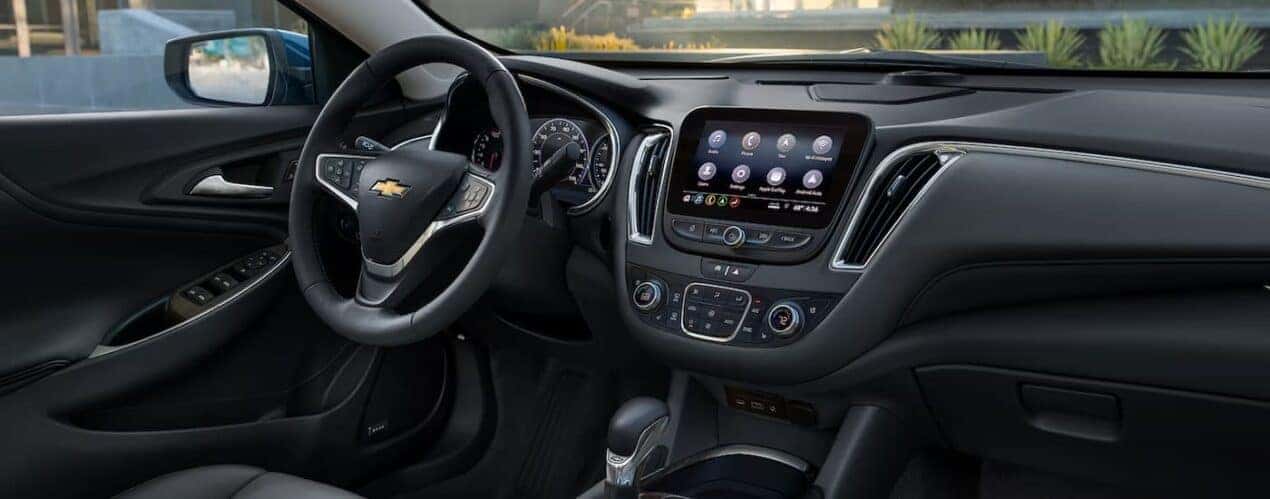 The black interior of a 2024 Chevy Malibu shows the steering wheel and center console.
