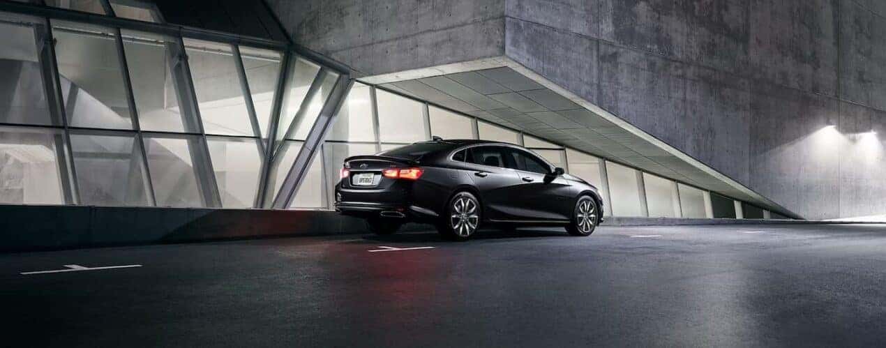 A black 2024 Chevy Malibu RS is shown from a rear angle parked near a building.
