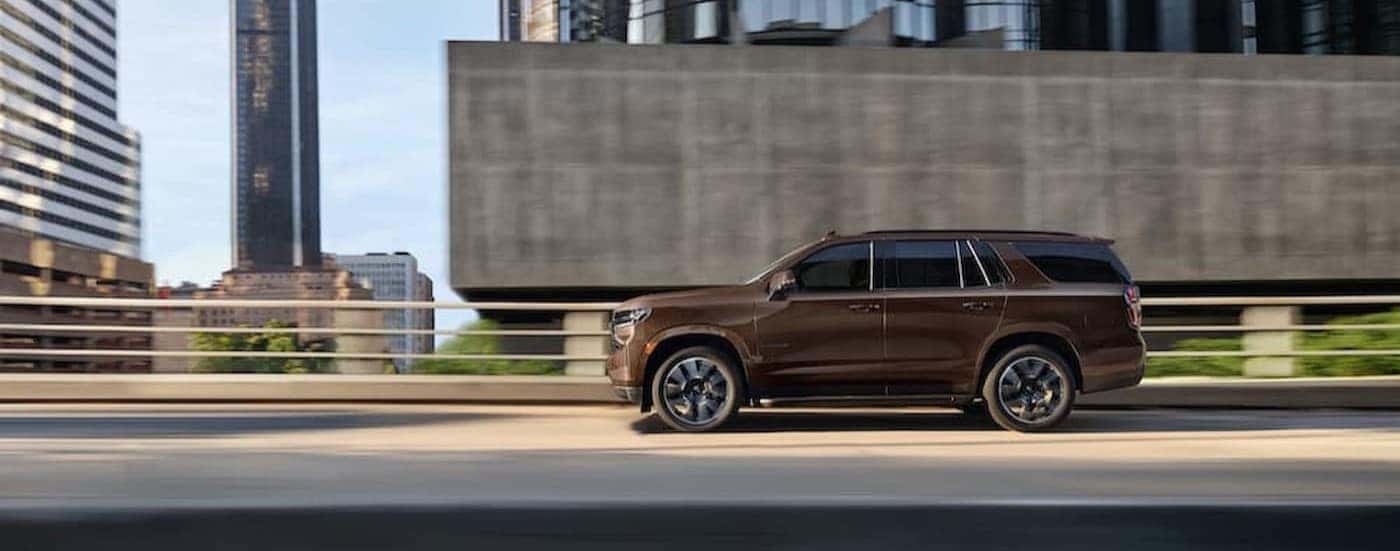 A brown 2022 Chevy Tahoe is shown driving on a city street.