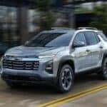 A silver 2025 Chevy Equinox is shown driving on a city street.