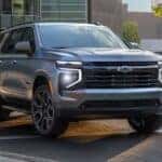 A silver 2025 Chevy Tahoe Z71 is shown driving near buildings.