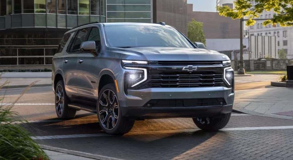 A silver 2025 Chevy Tahoe Z71 is shown driving near buildings.