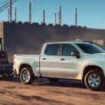 A white 2024 Chevy Silverado 1500 WT towing heavy machinery through a construction site.