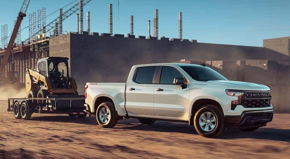 A white 2024 Chevy Silverado 1500 WT towing heavy machinery through a construction site.