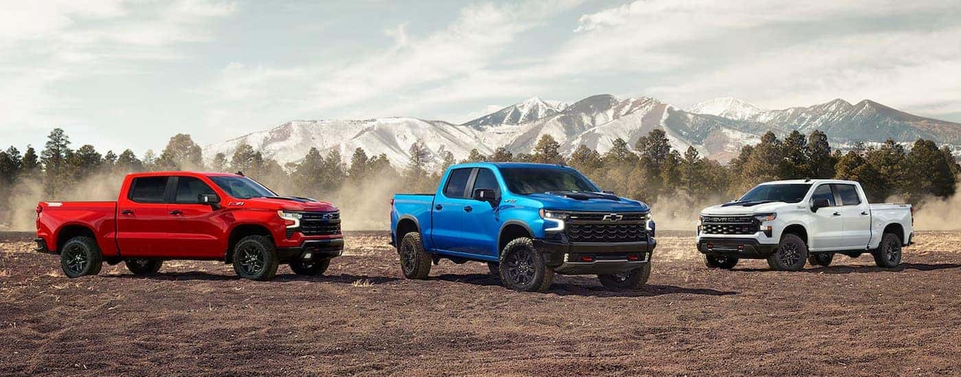 A group of three 2024 Chevy Silverados are parked on dirt.