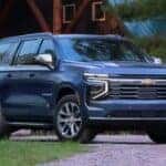 A grey 2025 Chevy Suburban is shown parked near a cabin.