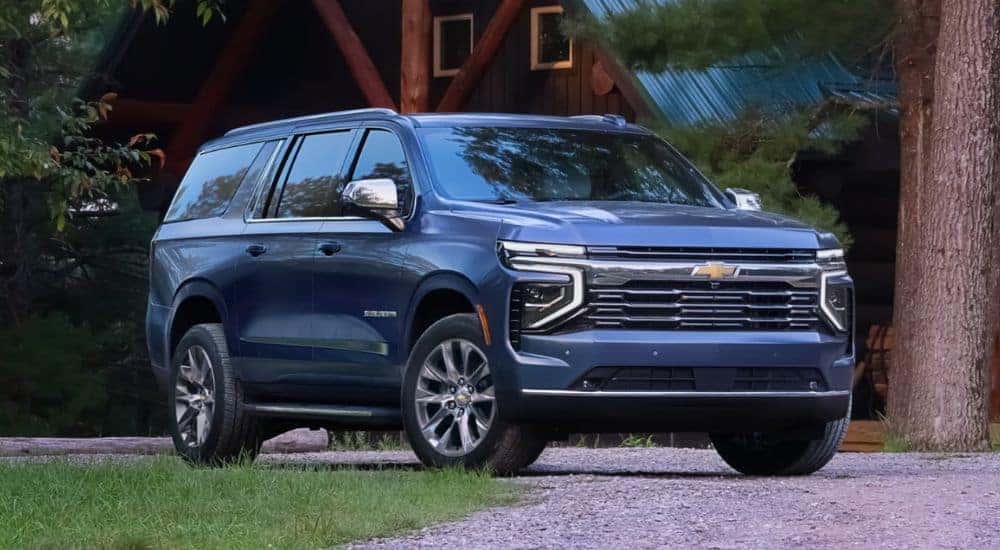 A grey 2025 Chevy Suburban is shown parked near a cabin.