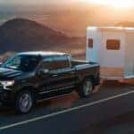 A black 2024 Chevy Silverado 1500 High Country towing a trailer on a coastal highway.