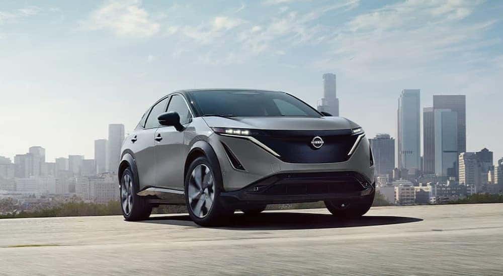 A gray 2024 Nissan ARIYA Platinum is shown driving near a city.