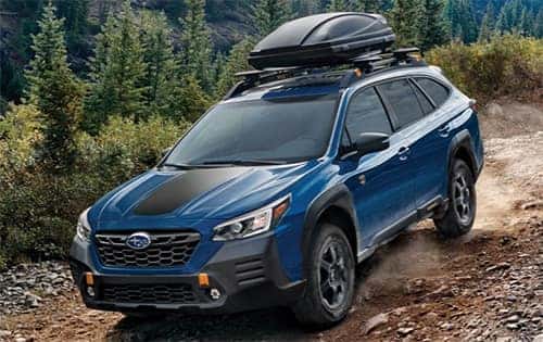 A Subaru vehicle driving down a dirt road with accessories attached to it.