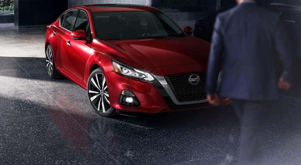 A man is walking toward a red 2021 Nissan Altima parked in a dim area after leaving an Indiana Nissan dealer.