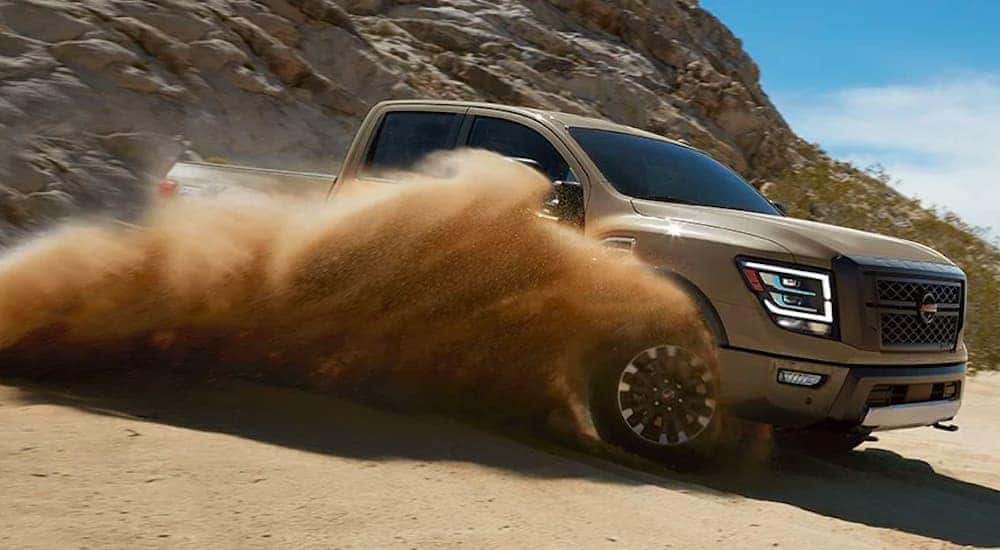 A brown 2020 Nissan Titan is driving down a dirt path kicking up dust.