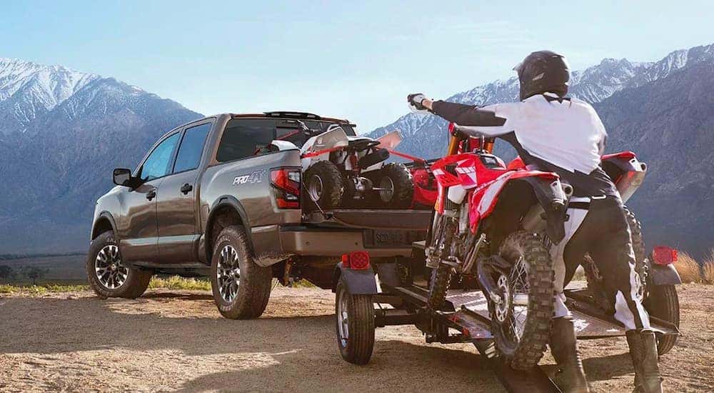 A black 2020 Nissan Titan Pro 4X is shown from behind with a ATV in the bed and a dirt bike being loaded on a trailer.