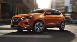 An orange 2020 Nissan Rogue Sport from a Louisville used Nissan dealer is driving on a city street.