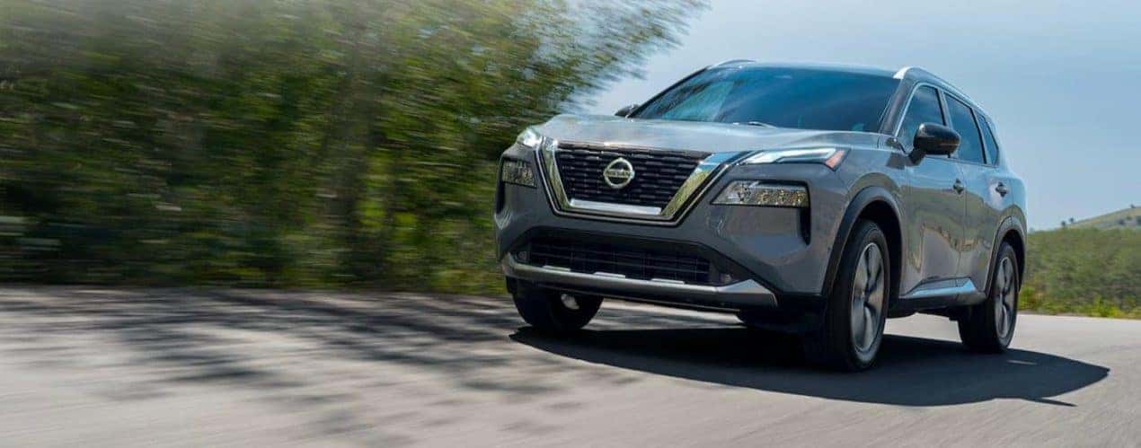 A grey 2021 Nisan Rogue is shown driving down a tree lined road after winning the 2021 Nissan Rogue vs 2021 Ford Escape comparison.