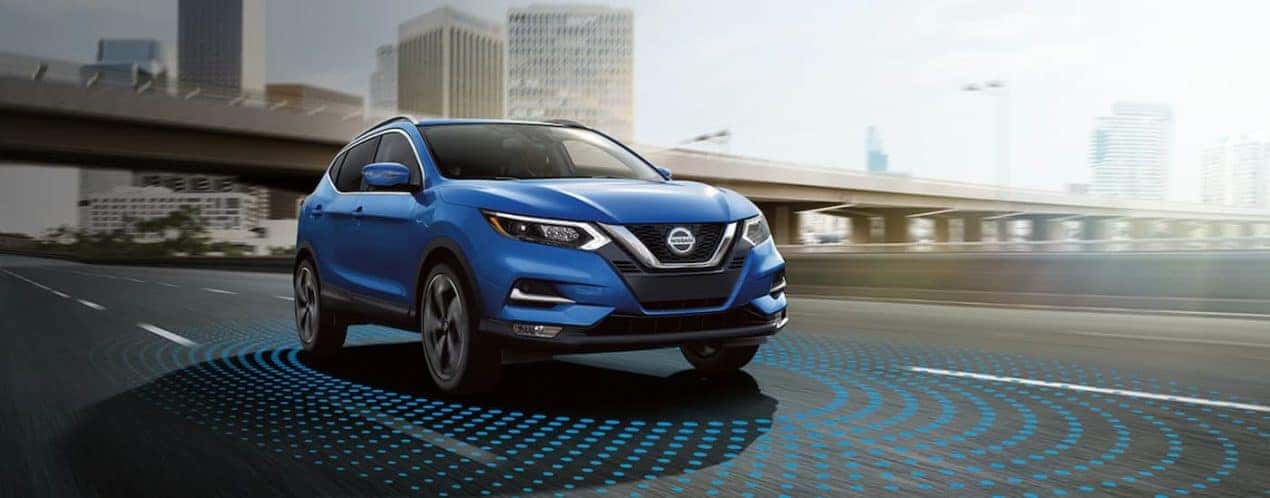 A blue 2021 Nissan Rogue Sport is shown driving past a city with simulated sensor lines.