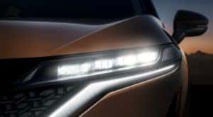 A close up shows the headlight on a bronze 2022 Nissan Ariya.