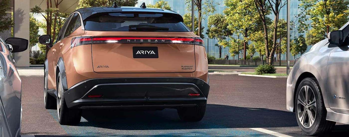 A bronze 2022 Nissan Ariya is shown reversing into a parking space.