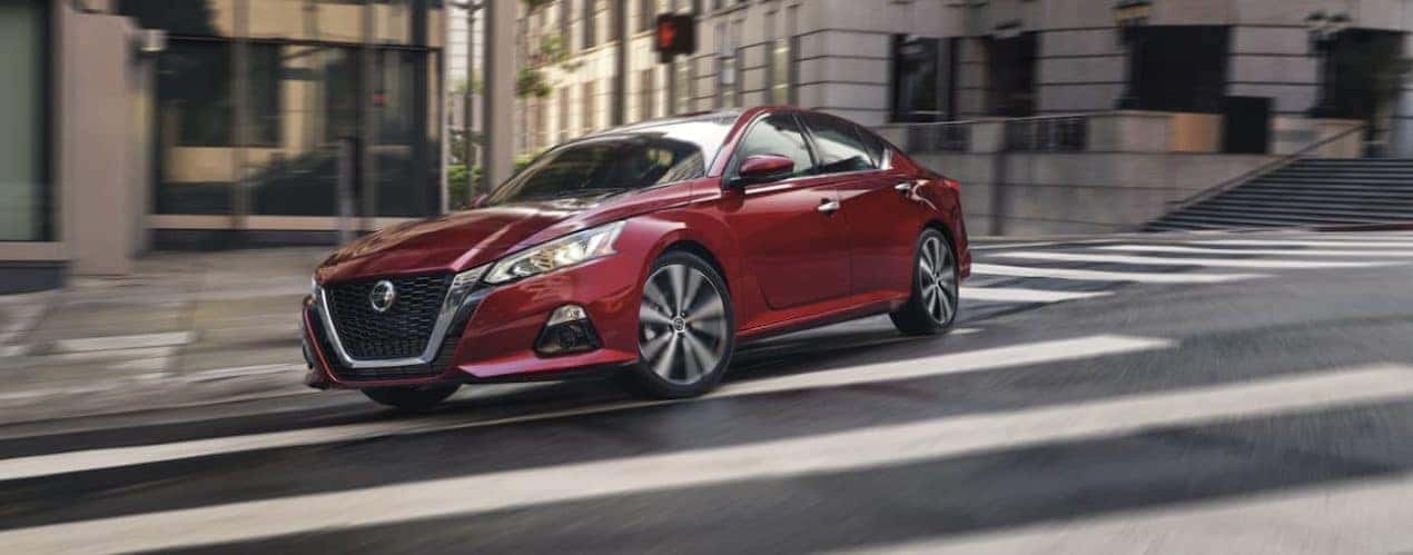 A red 2021 Nissan Altima is shown rounding a corner in a city.